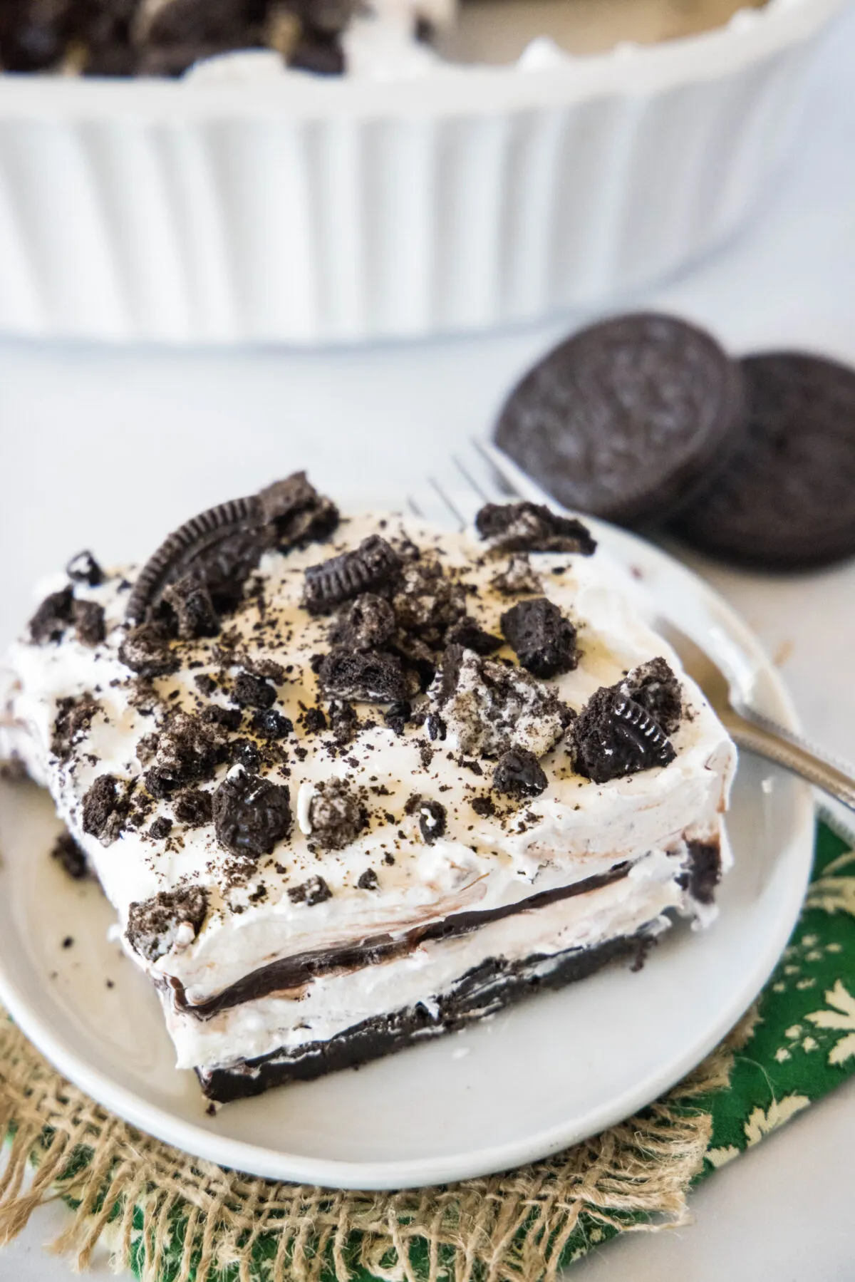 Overhead view of a slice of Oreo squares on a plate, topped with crumbled Oreos, next to a few Oreos