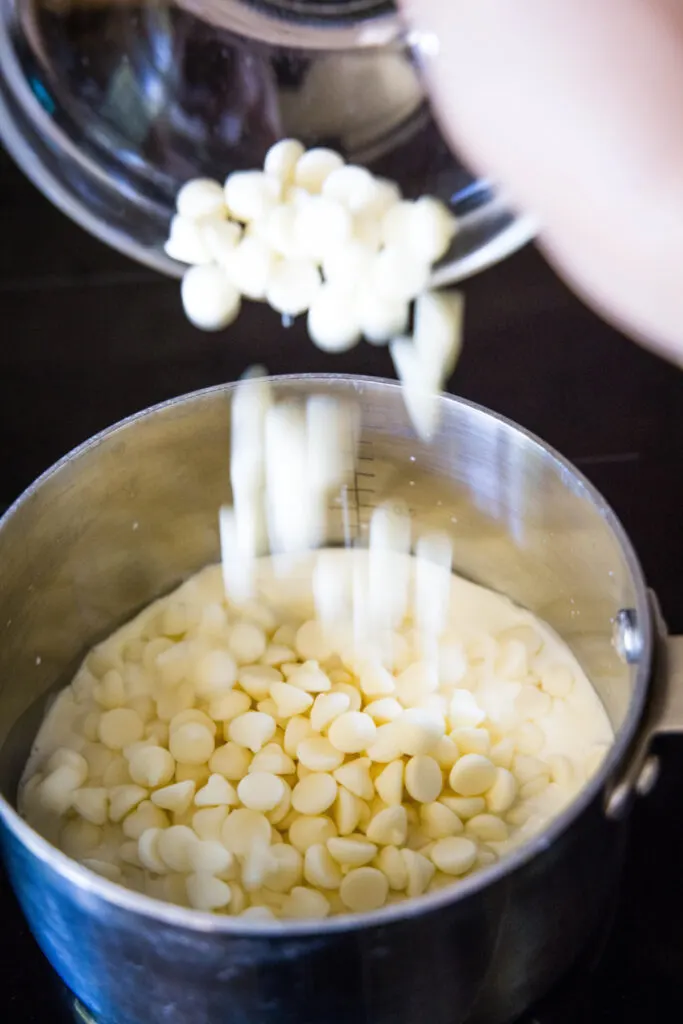 White chocolate chips being poured into a saucepan with cream