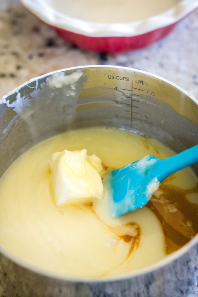 Butter melting in a saucepan with vanilla, cream, and white chocolate, with a rubber spatula