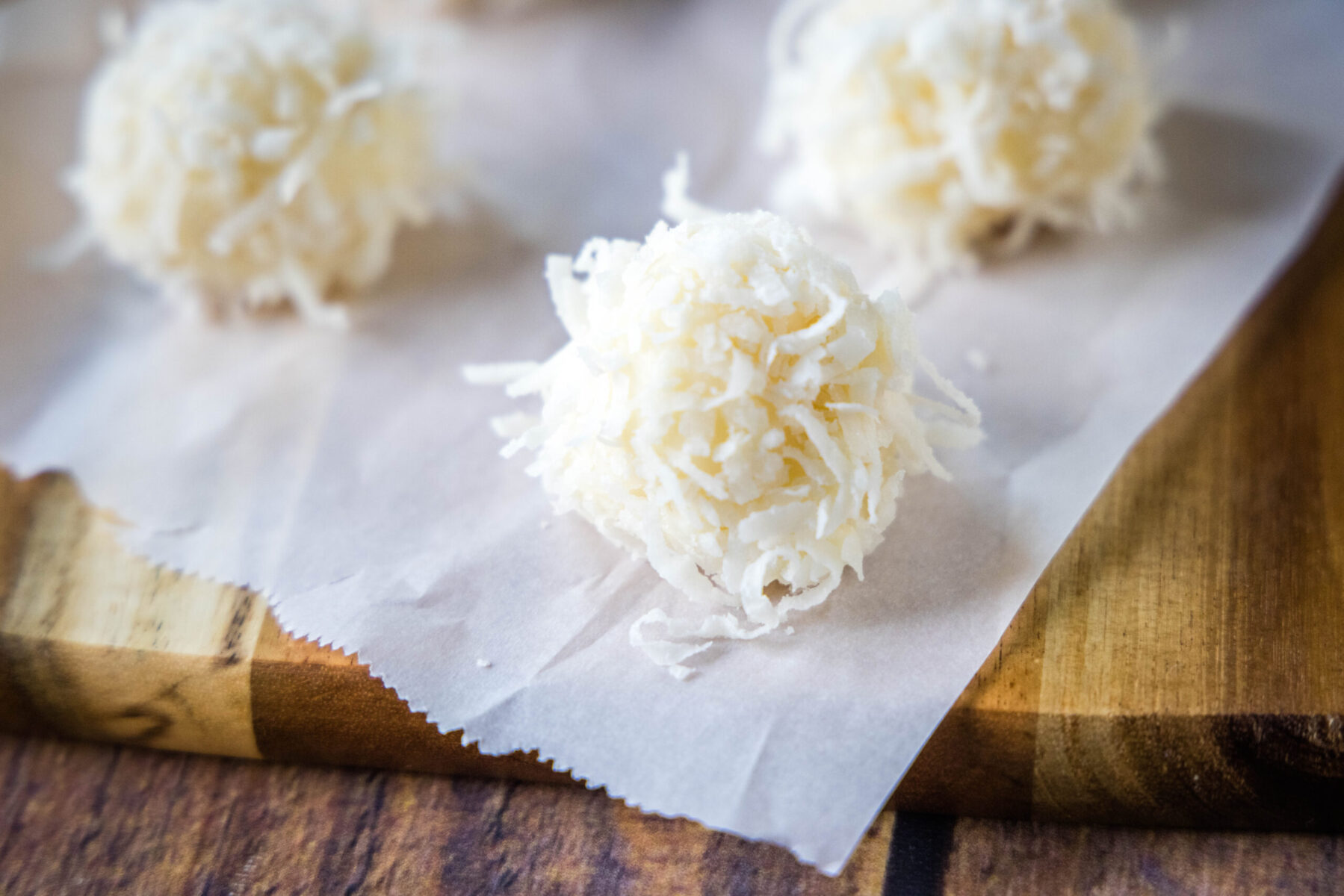 Close up of white chocolate truffles with coconut on a piece of parchment paper