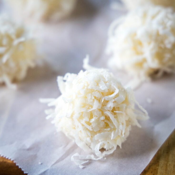Close up of a white chocolate truffle topped with coconut next to others
