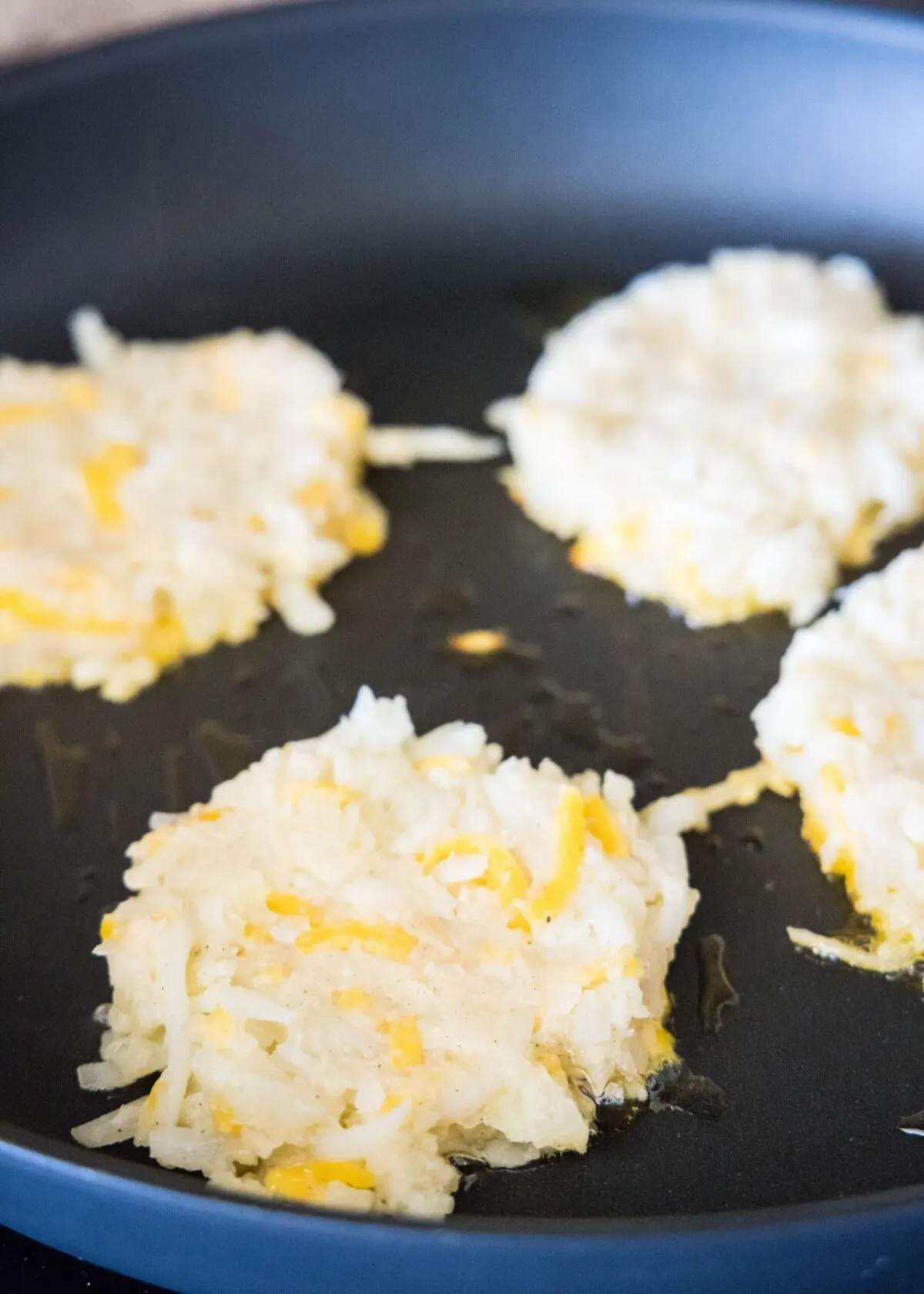 Four uncooked cauliflower fritters in a skillet
