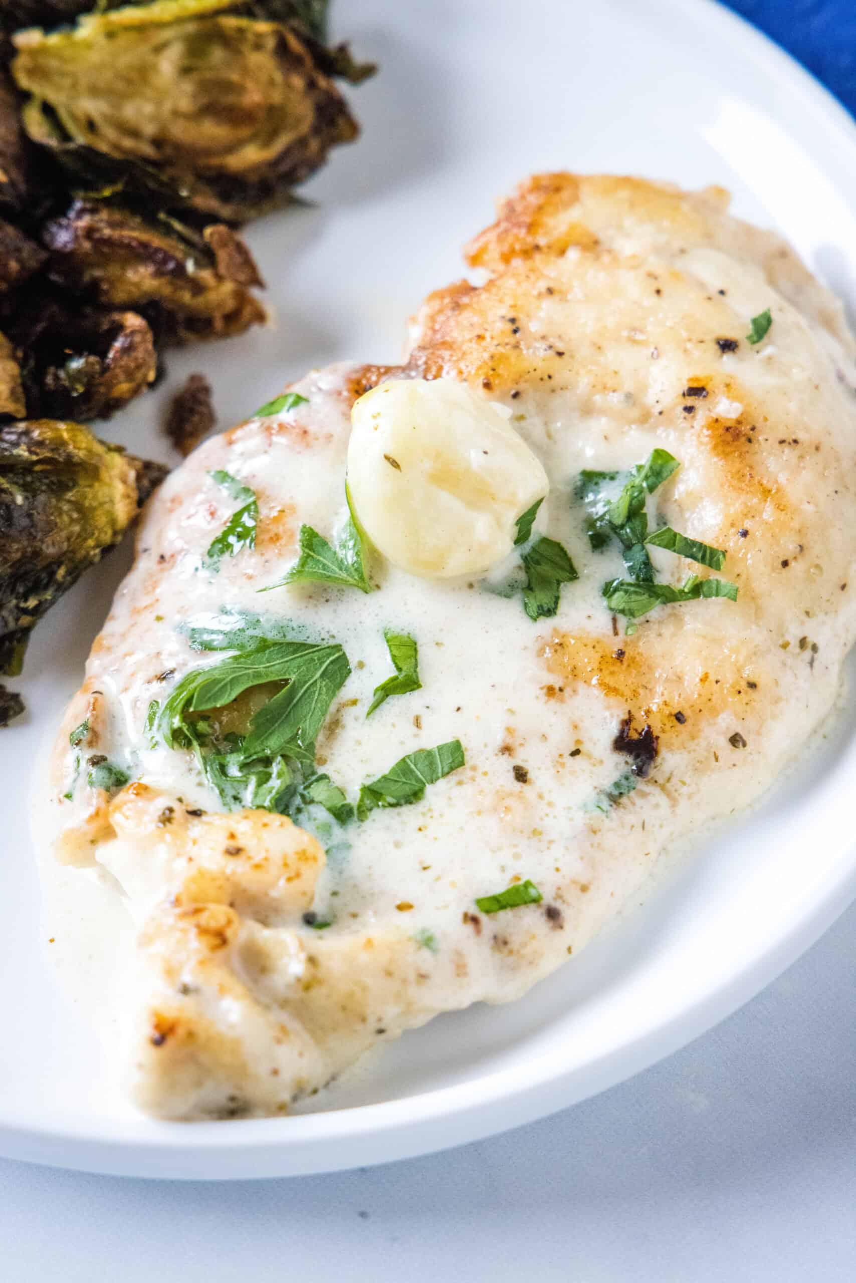 This one-pan creamy garlic chicken with golden, pan-seared chicken breasts in a rich garlic sauce is an easy dinner, ready in 30 minutes! Overhead view of creamy garlic chicken served with a side of roasted Brussels sprouts on a plate.
