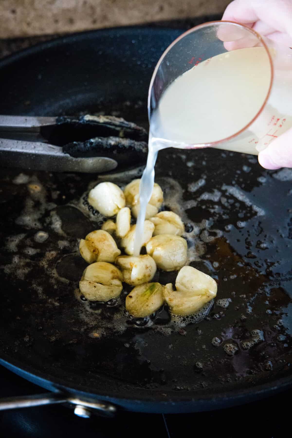 This one-pan creamy garlic chicken with golden, pan-seared chicken breasts in a rich garlic sauce is an easy dinner, ready in 30 minutes! Chicken broth being poured into a skillet with sautéed garlic cloves.