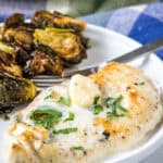 Creamy garlic chicken served with a side of roasted Brussels sprouts on a plate.