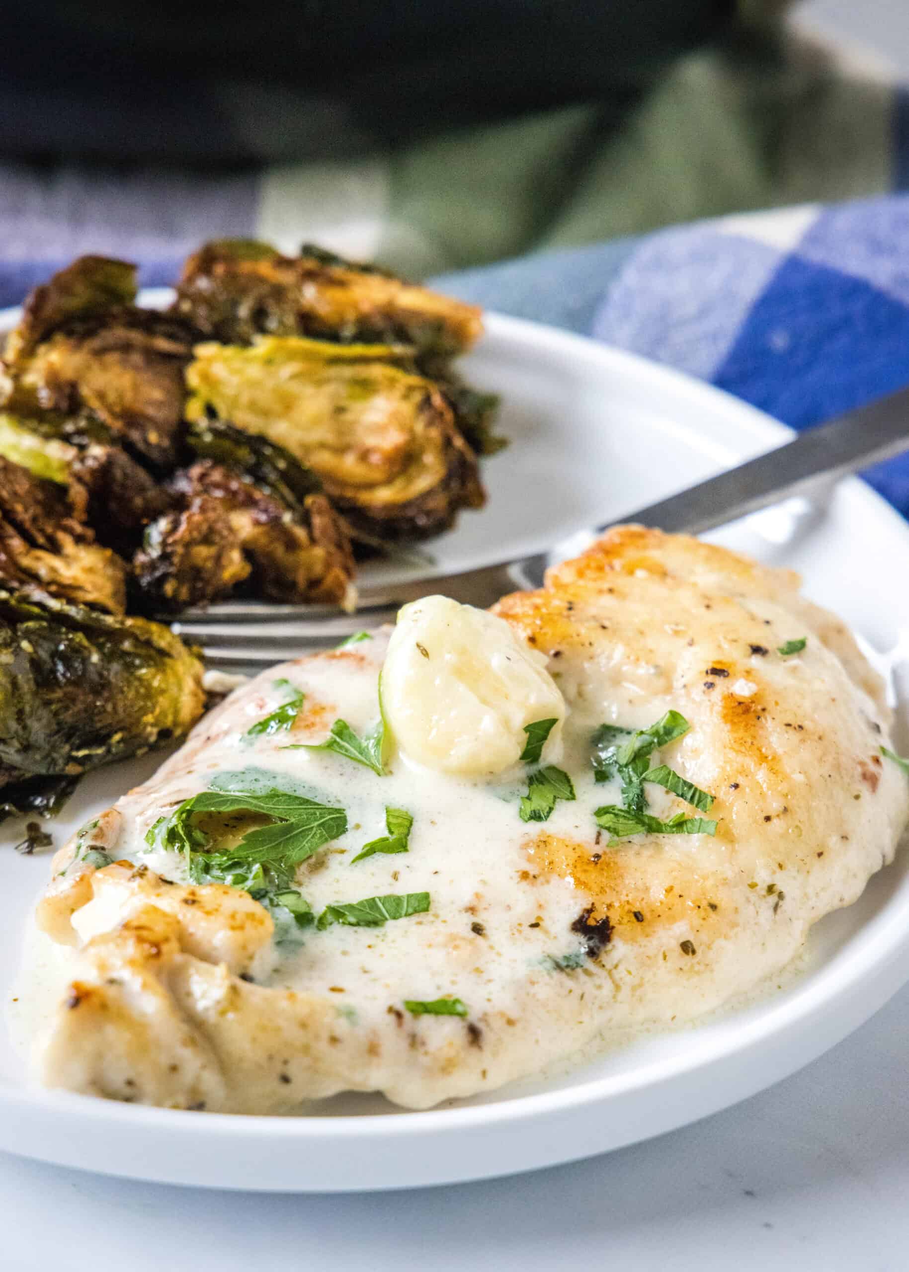 This one-pan creamy garlic chicken with golden, pan-seared chicken breasts in a rich garlic sauce is an easy dinner, ready in 30 minutes! Creamy garlic chicken served with a side of roasted Brussels sprouts on a plate.