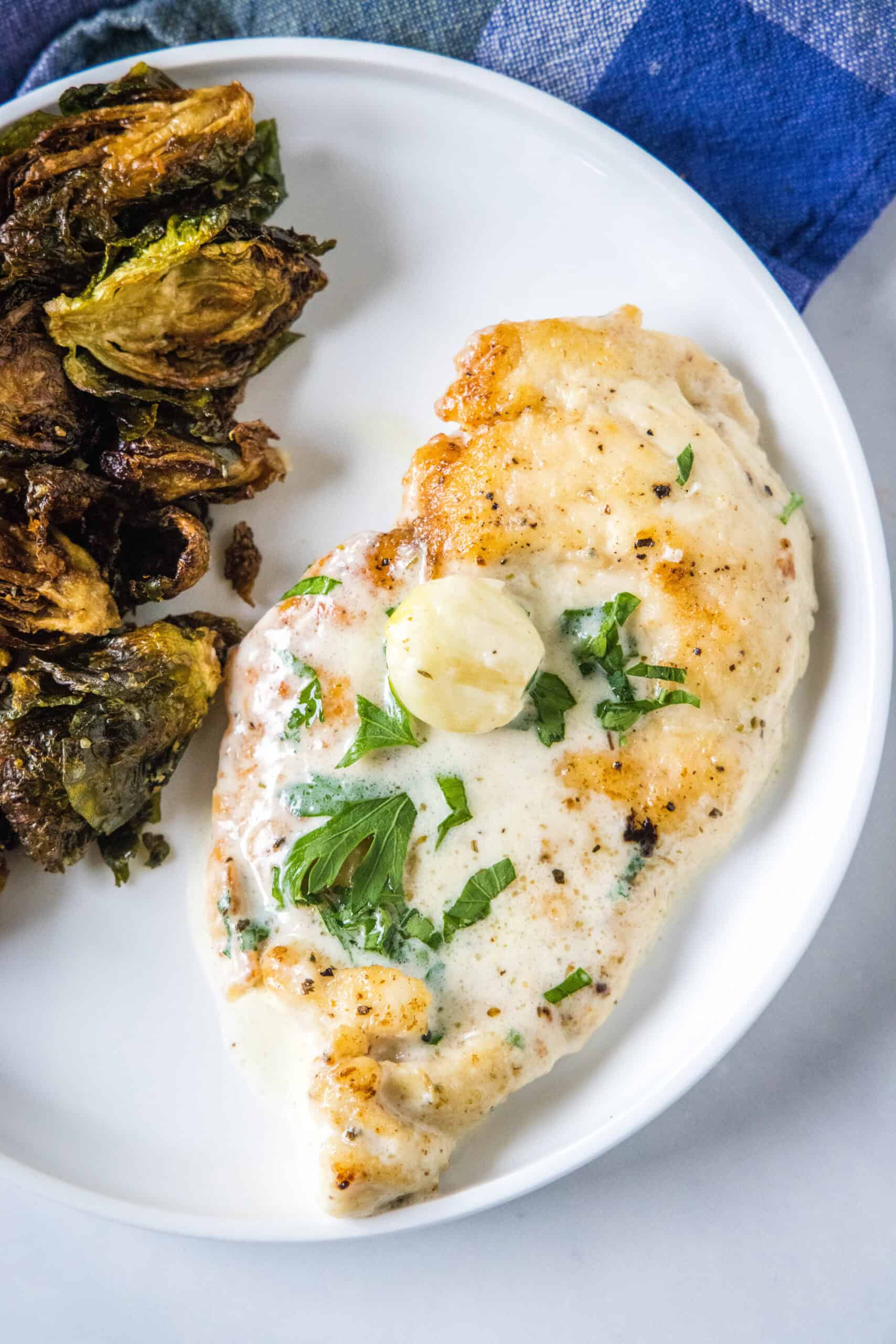 This one-pan creamy garlic chicken with golden, pan-seared chicken breasts in a rich garlic sauce is an easy dinner, ready in 30 minutes! Overhead view of creamy garlic chicken served with a side of roasted Brussels sprouts on a plate.