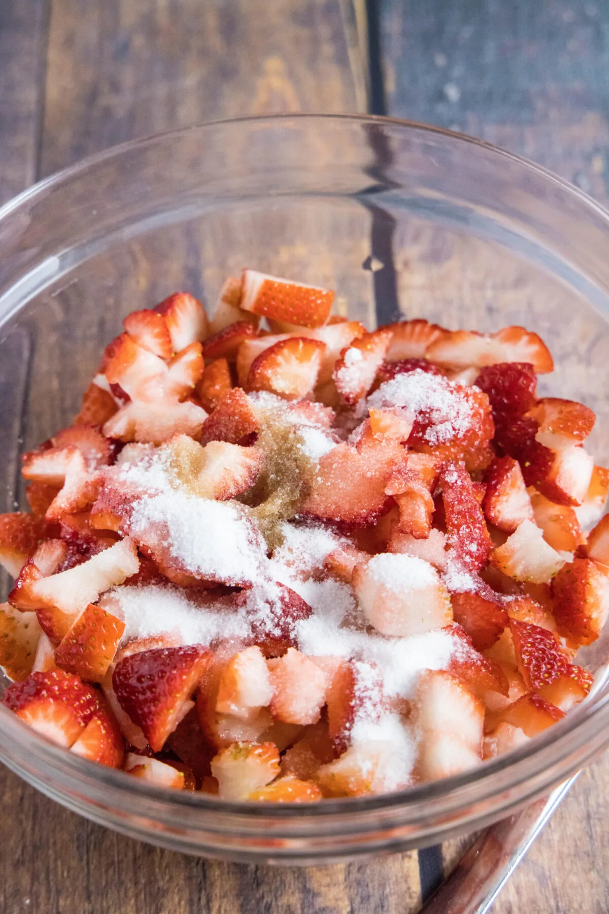 A mixing bowl with sliced strawberries, sugar, and vanilla