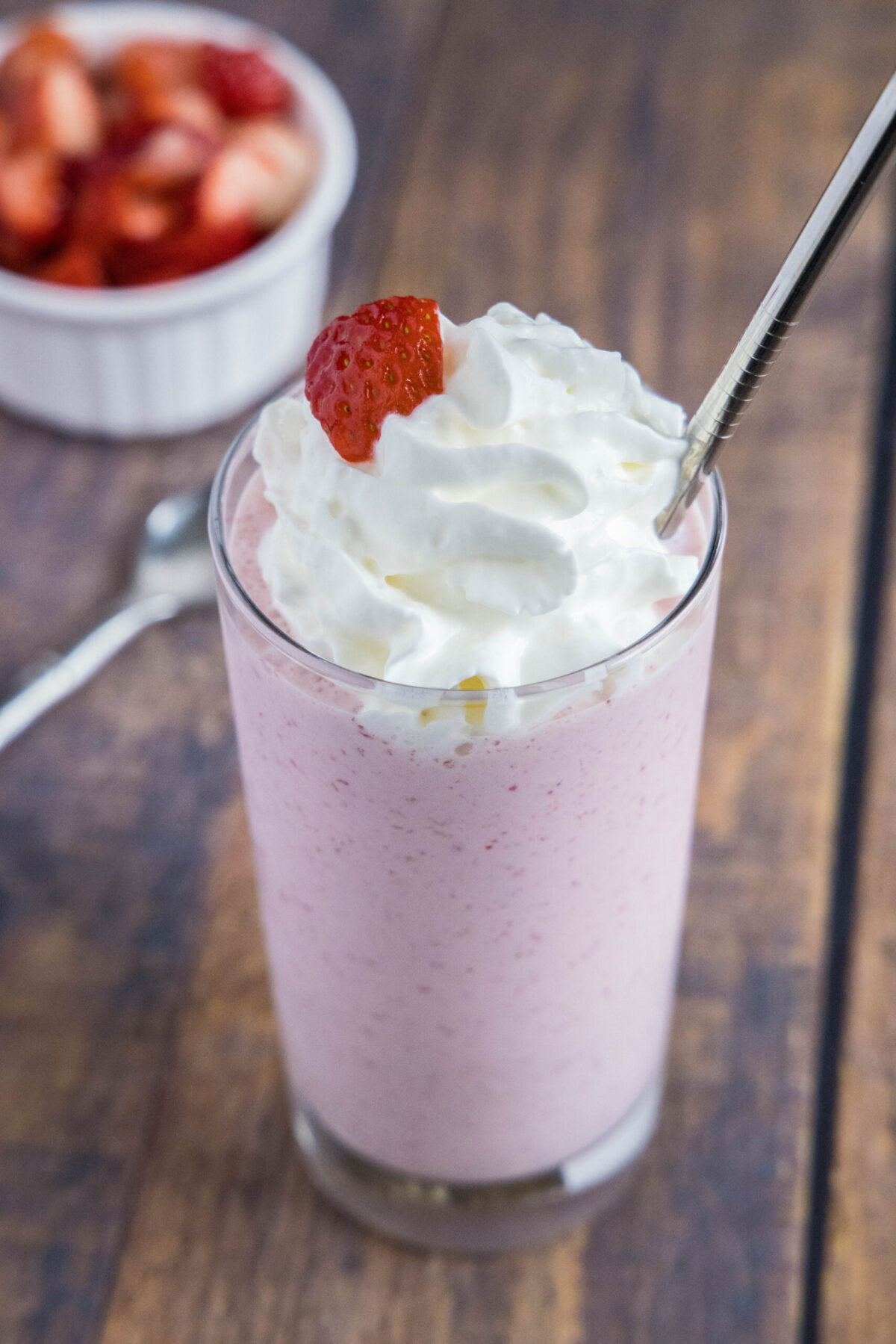 Overhead view of a strawberry milkshake with whipped cream, with a bowl of strowberries in the background.