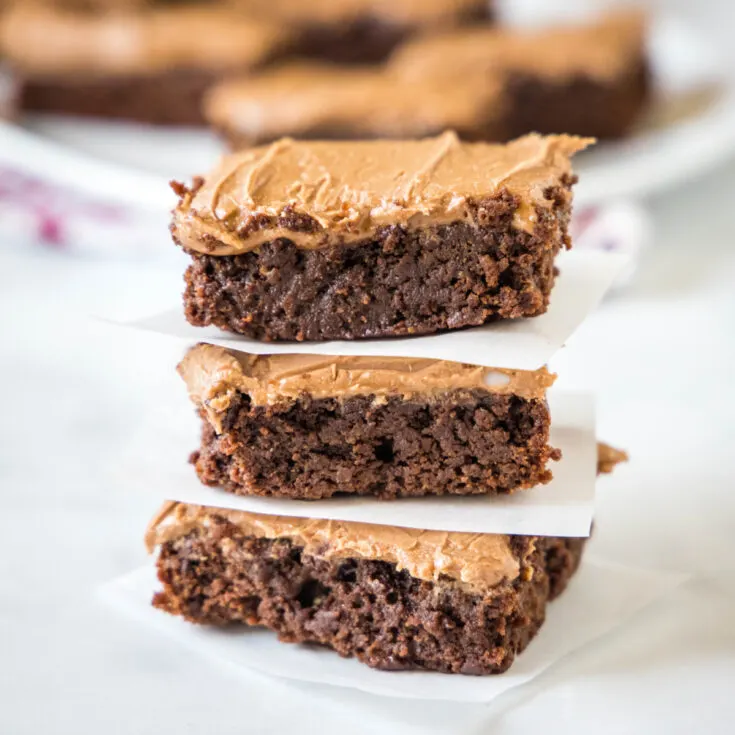 Three brownie squares with frosting stacked on top of each other.