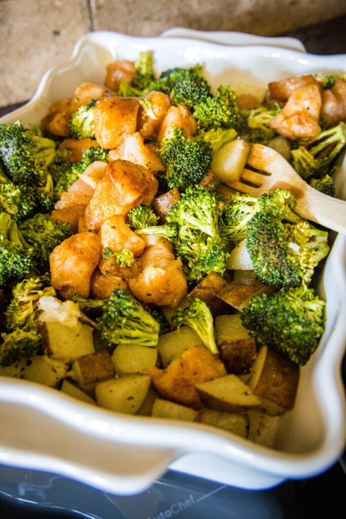 A casserole dish with broccoli, potatoes, and chicken, with a wooden spoon.