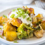Close up of a plate of chicken, broccoli, and potato casserole topped with sour cream and green onions.