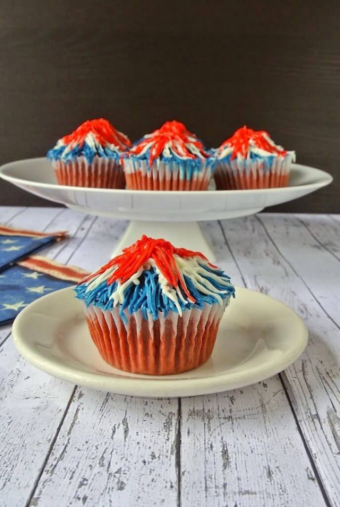 Memorial Day Firework Cupcakes on a cake stand with one plated cupcake in the foreground