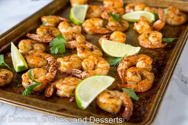 A tray of baked shrimp with lime wedges
