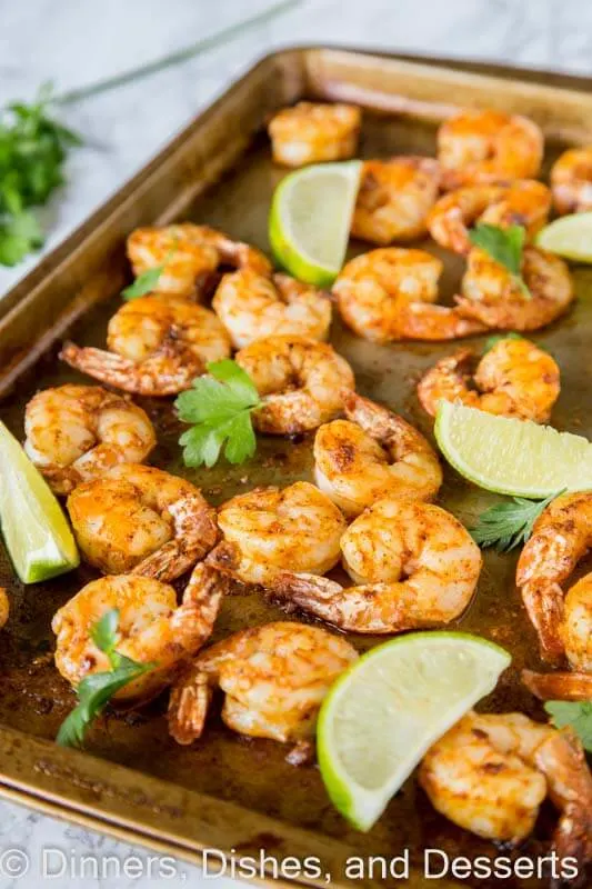 sheet pan of baked shrimp with lime wedges