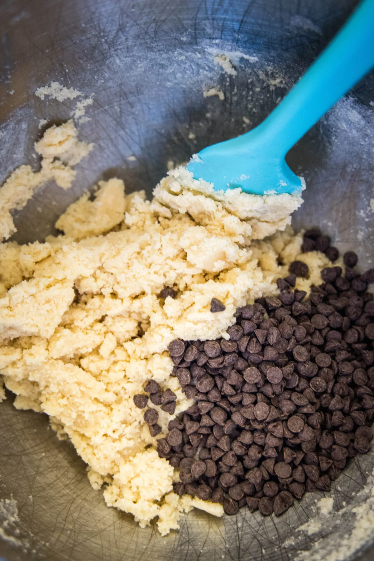 A mixing bowl with shortbread dough, chocolate chips, and a spatula.