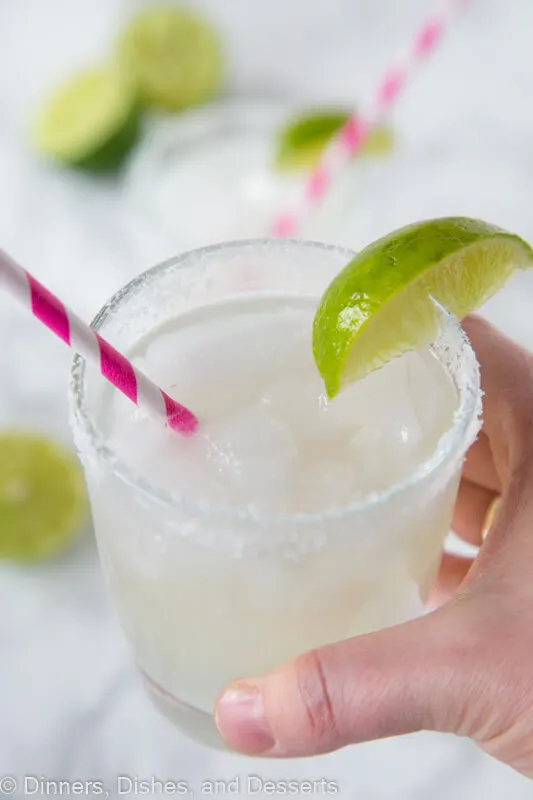 hand holding margarita in a glass with lime wedge and pink straw