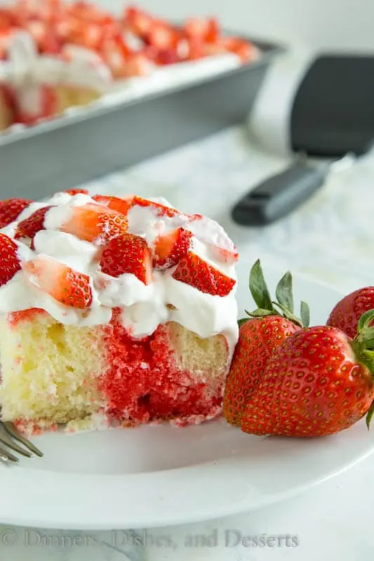 Strawberry poke cake topped with fresh strawberries and fresh whipped cream