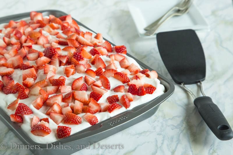 Poke cake in a pan with homemade whipped cream and lots of fresh strawberries