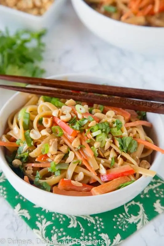 A bowl of peanut noodles and vegetables with chopsticks