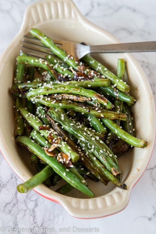 roasted green beans in a dis with sesame seeds and a fork