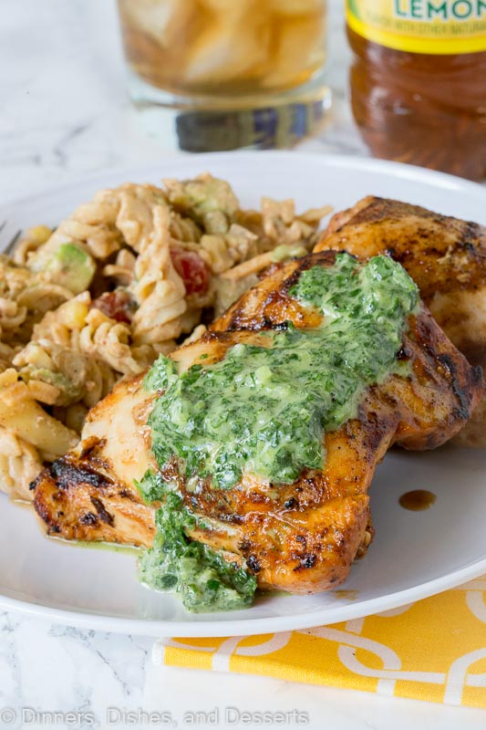 A plate of grilled chicken with herb sauce on top