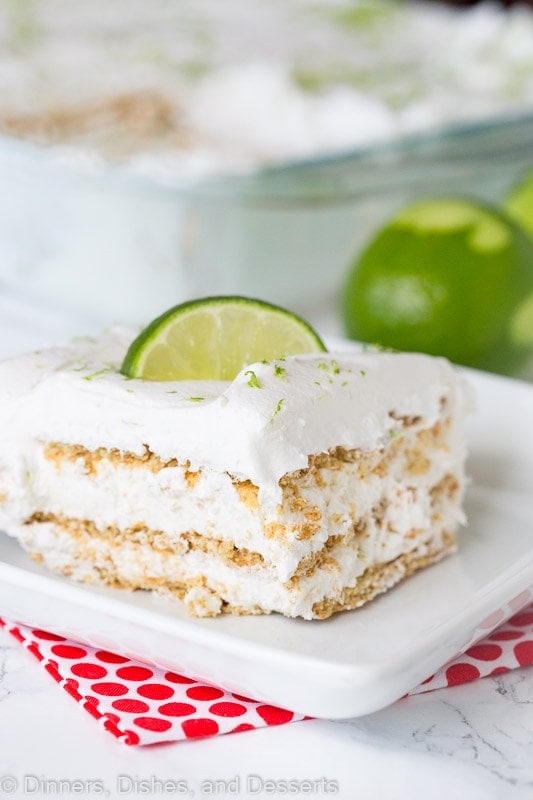 A piece of key lime ice box cake sitting on a plate with limes in the background