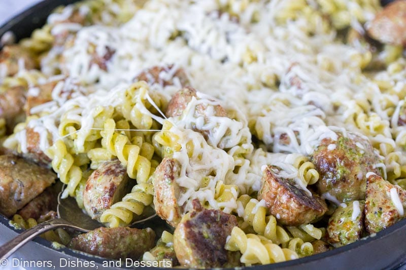 skillet with pesto pasta with meatballs topped with melted cheese