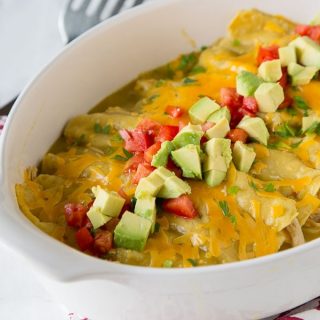 a dish of enchiladas topped with tomatoes and avocados