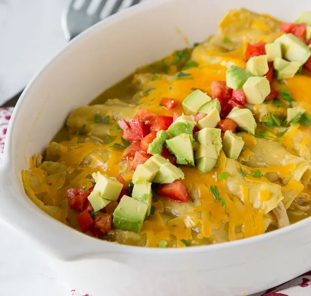 a dish of enchiladas topped with tomatoes and avocados
