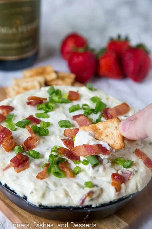 blue cheese dip topped with green onions and bacon in a dish with a cracker