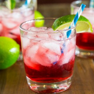 A glass of cranberry vodka on the table with limes