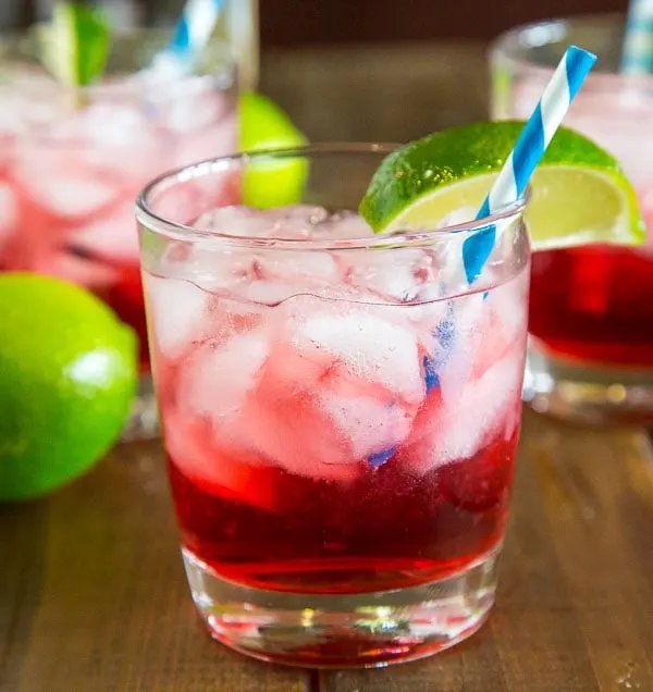 A glass of cranberry vodka on the table with limes