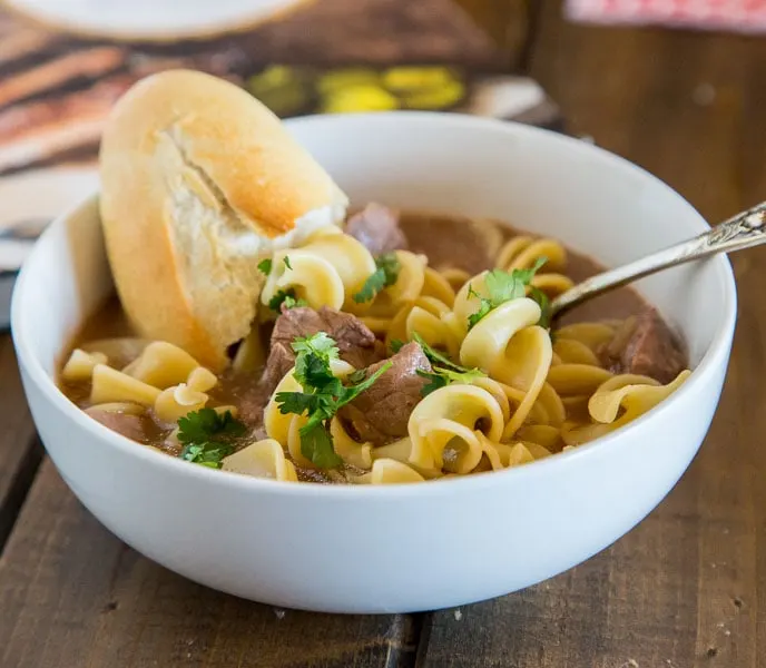 A bowl of beef and noodle soup with bread