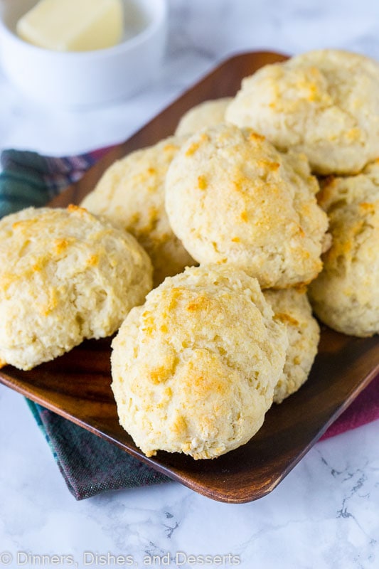 A wooden tray full of biscuits, with a bowl of butter in the background