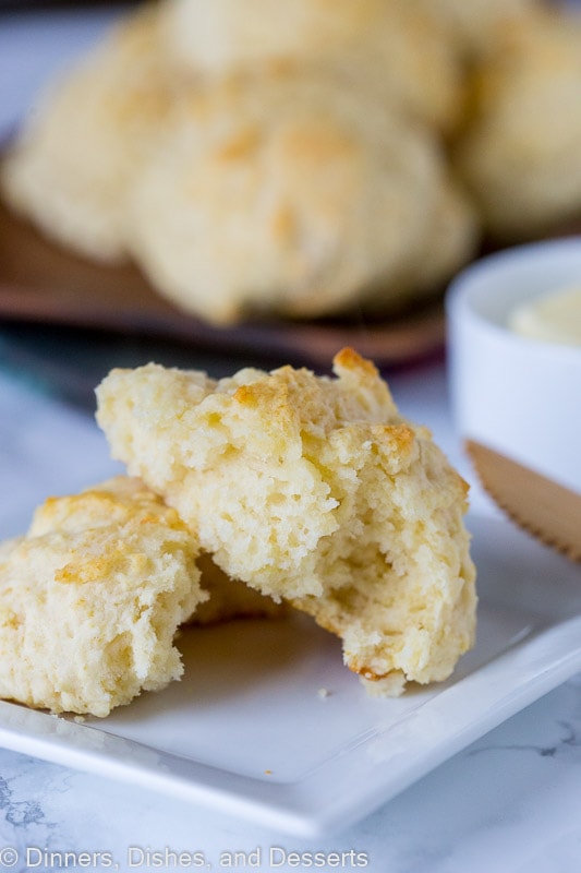 A plate with a biscuit on it broken in half, with a tray of biscuits in the background. 