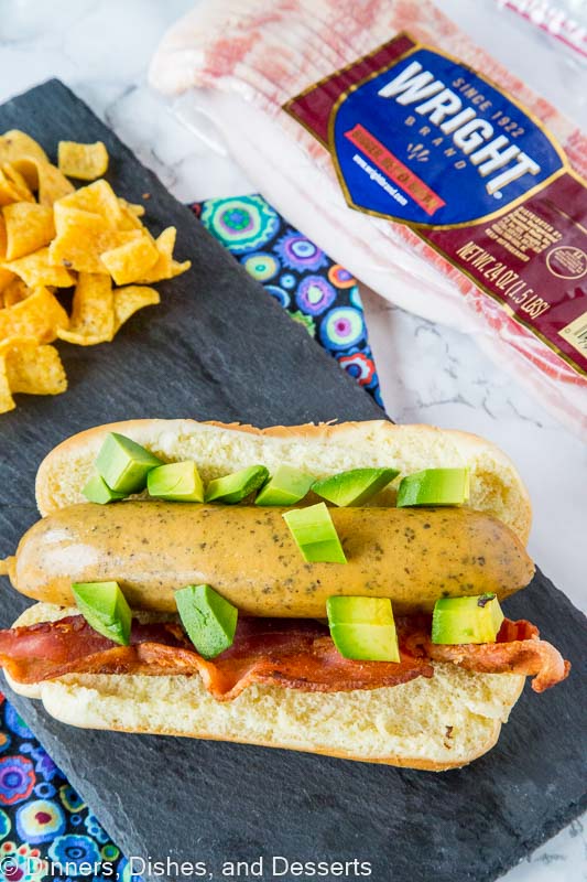 a brat with avocado and bacon on a board