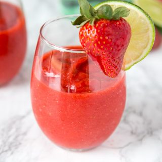 A glass of frozen strawberry daiquiri with a strawberry and lime slice