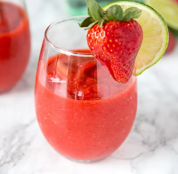 A glass of frozen strawberry daiquiri with a strawberry and lime slice