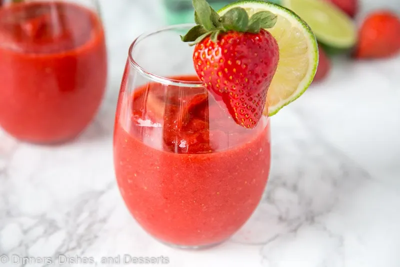 A glass of frozen strawberry daiquiri with a strawberry and lime slice