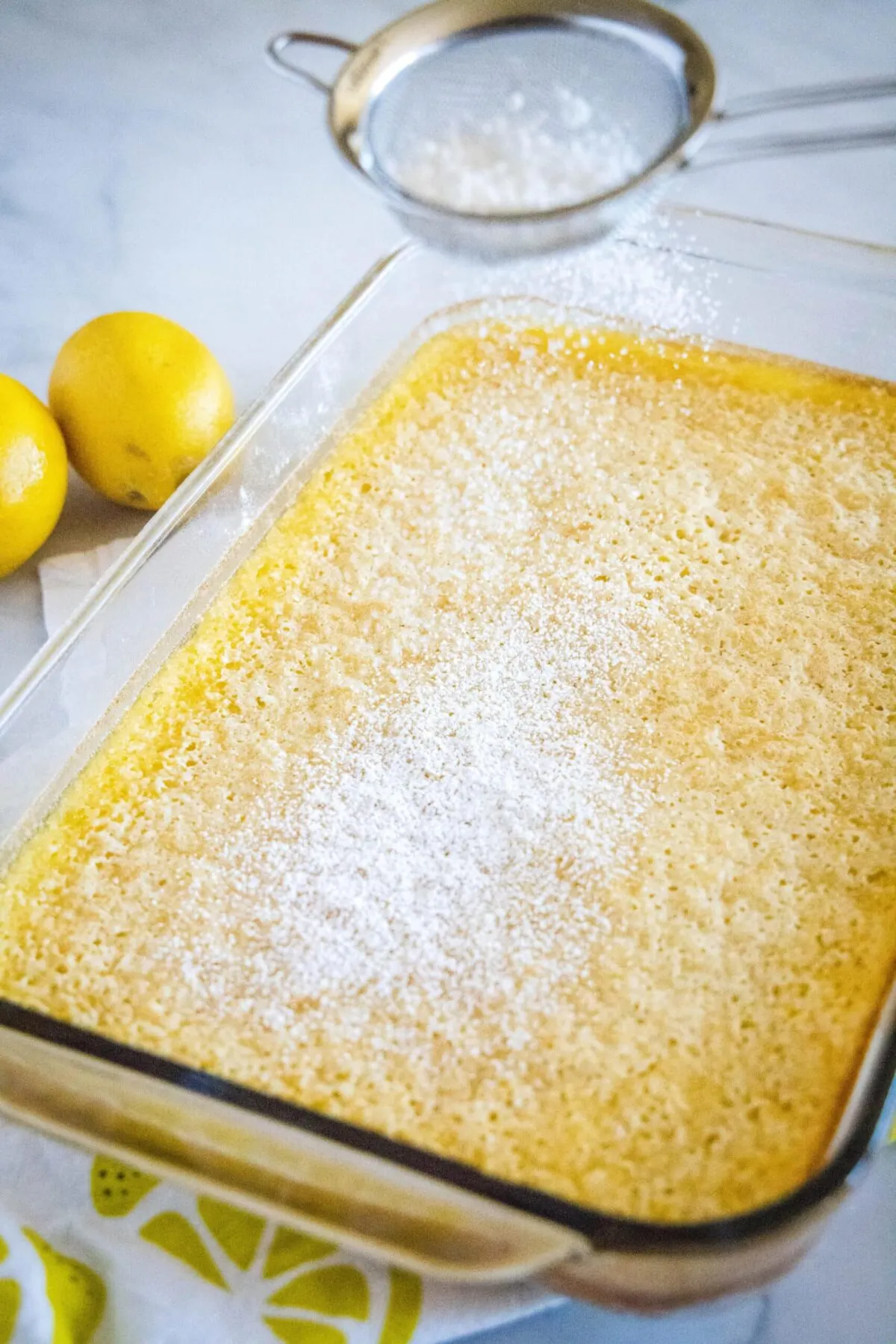 A baking pan full of lemon bars, with a sifter covering them with powdered sugar