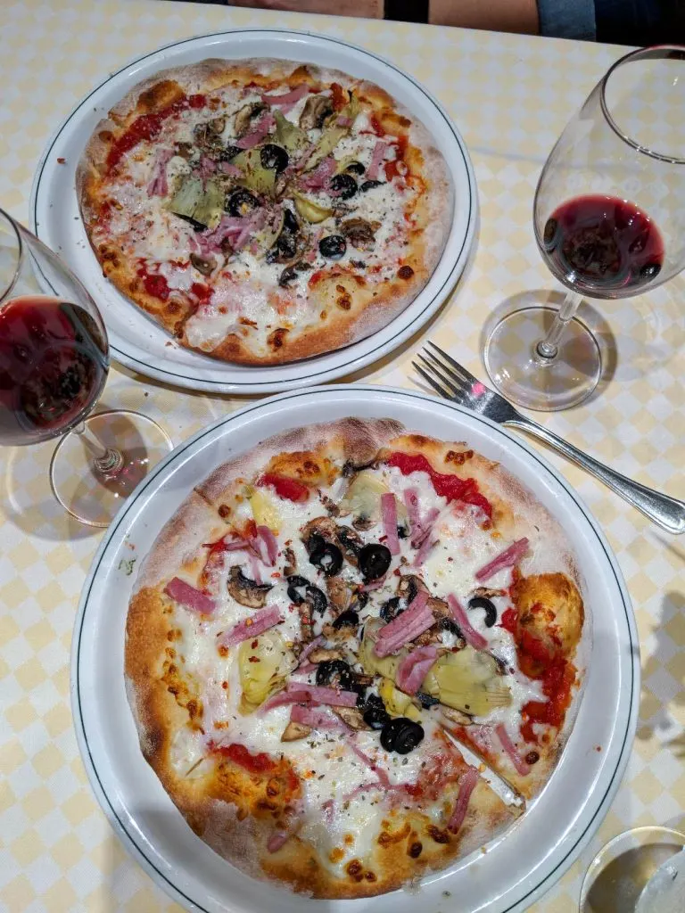 A pizza sitting on top of a plate of food on a table a glass of wine