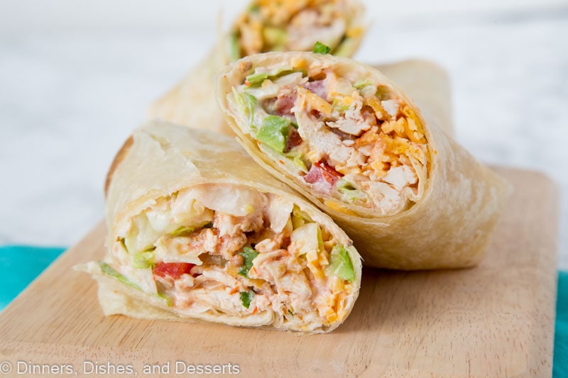A chicken wrap cut in half diagonally, with one half resting on top of the other, with another wrap in the background