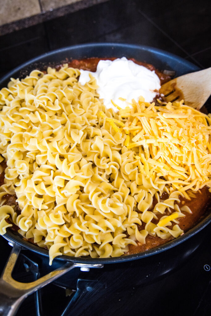 A skillet filled with egg noodles, sauce, cheese, and sour cream