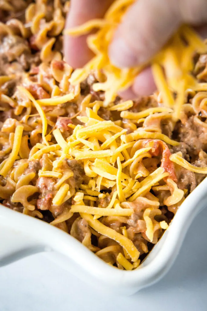 A hand placing shredded cheese in a casserole dish
