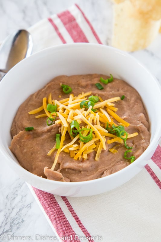 A bowl of refried beans topped with cheddar cheese and green onion