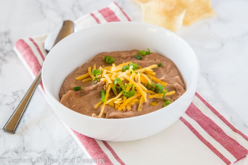 A bowl of refried beans topped with cheddar cheese, tortilla chips on the side