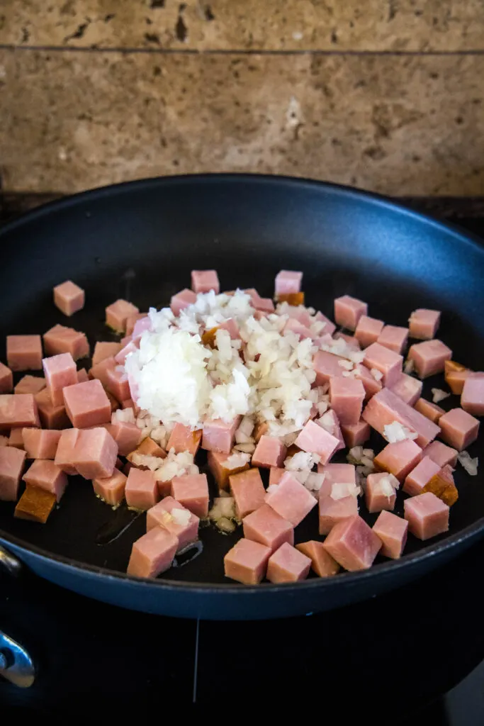 Seasonings added to sauteed ham and onions in a skillet.