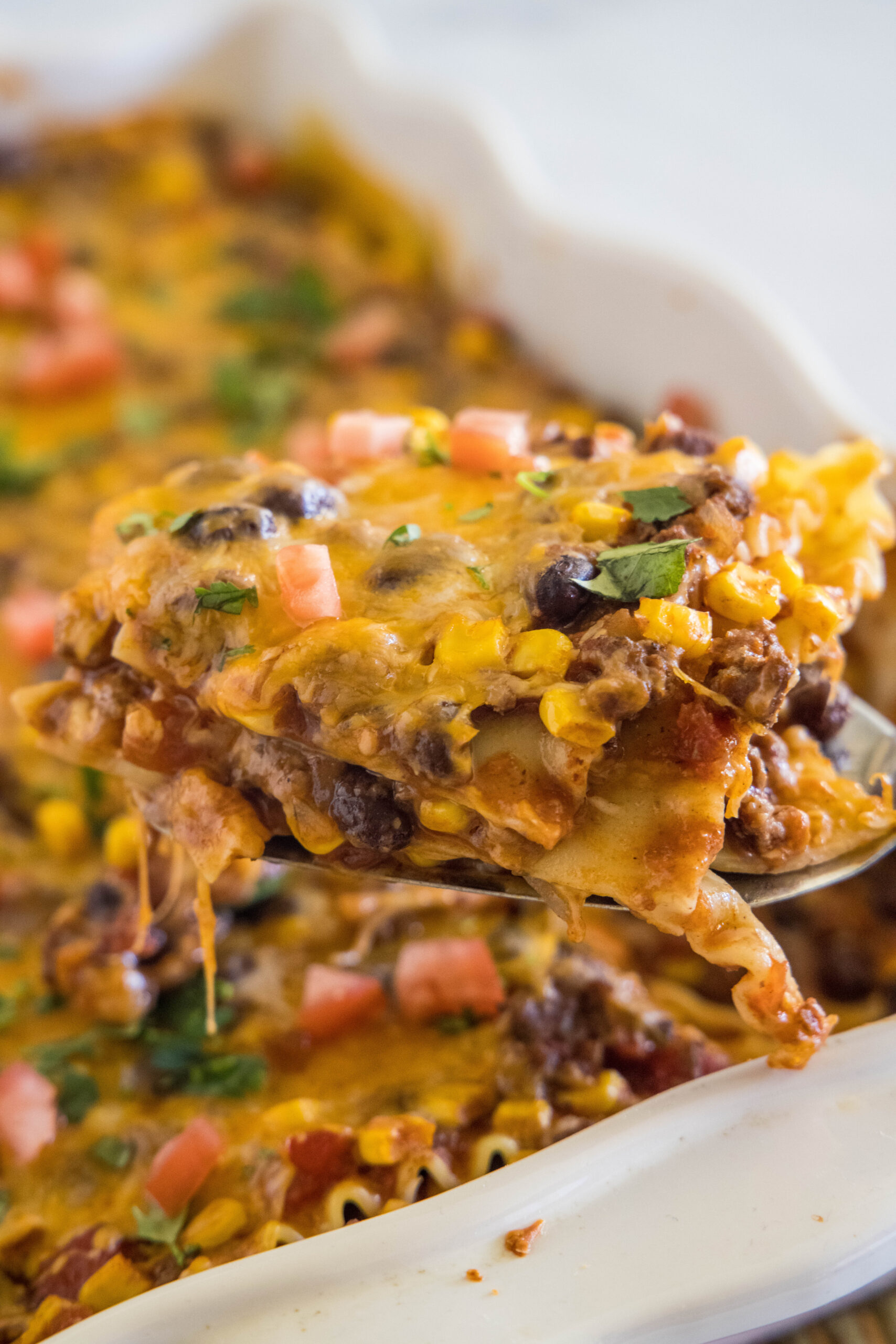 A slice of Mexican lasagna lifted from a ceramic baking dish.