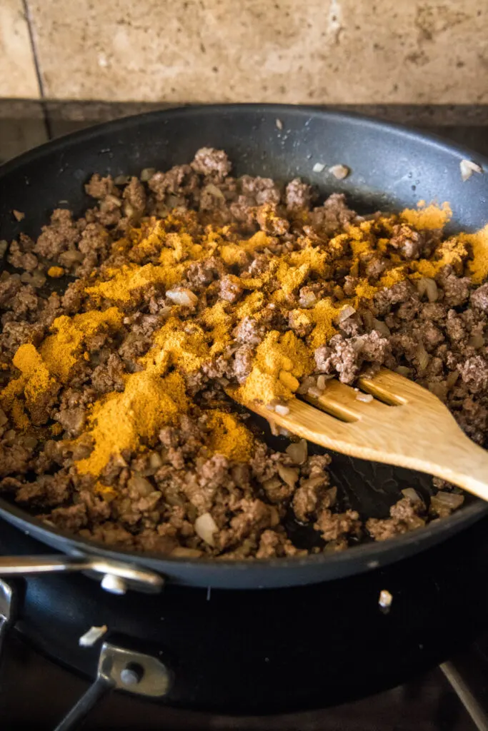 Browned ground beef topped with taco seasoning in a skillet with a wooden spatula.